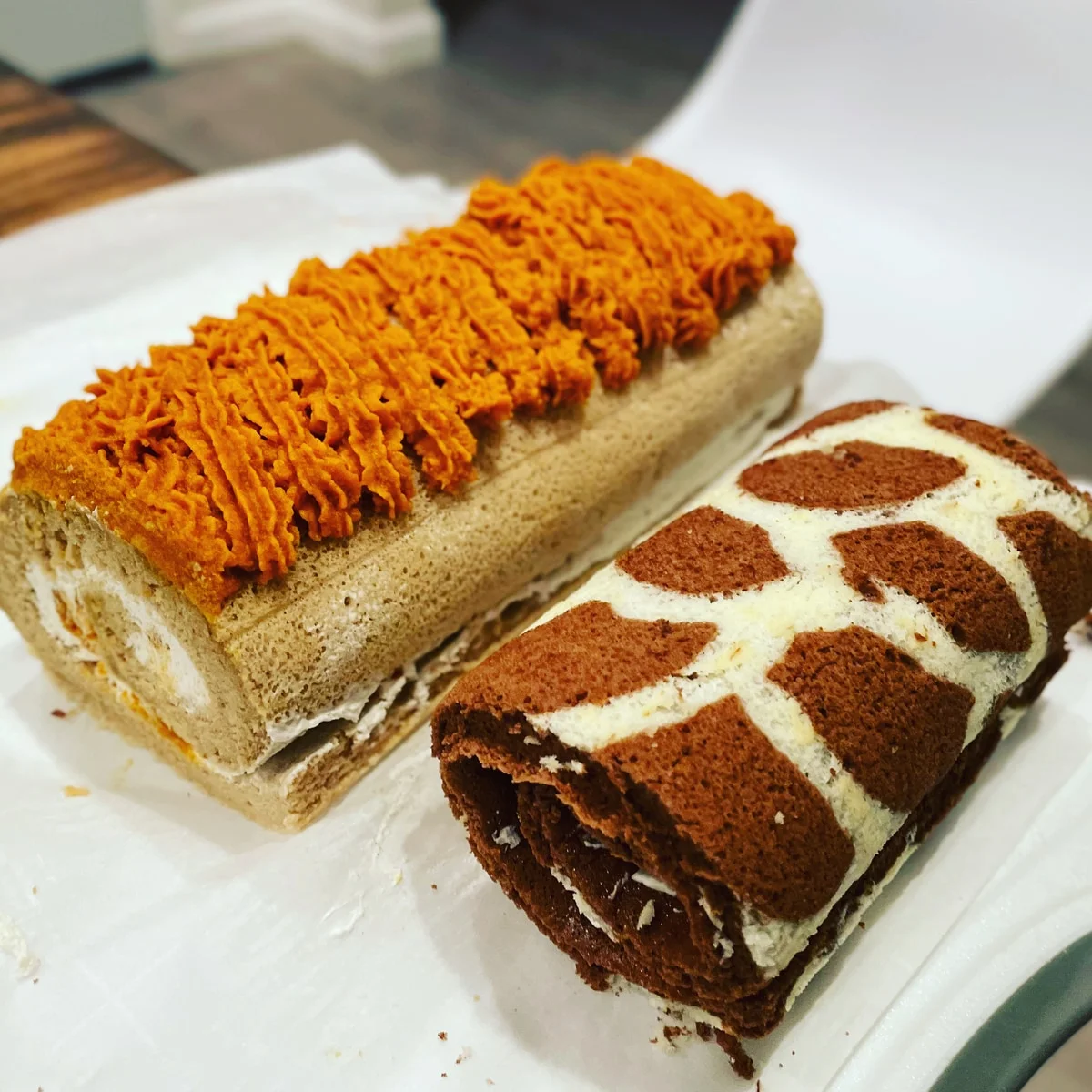 Two cake rolls, one with orange topping and one with a brown-and-white pattern.