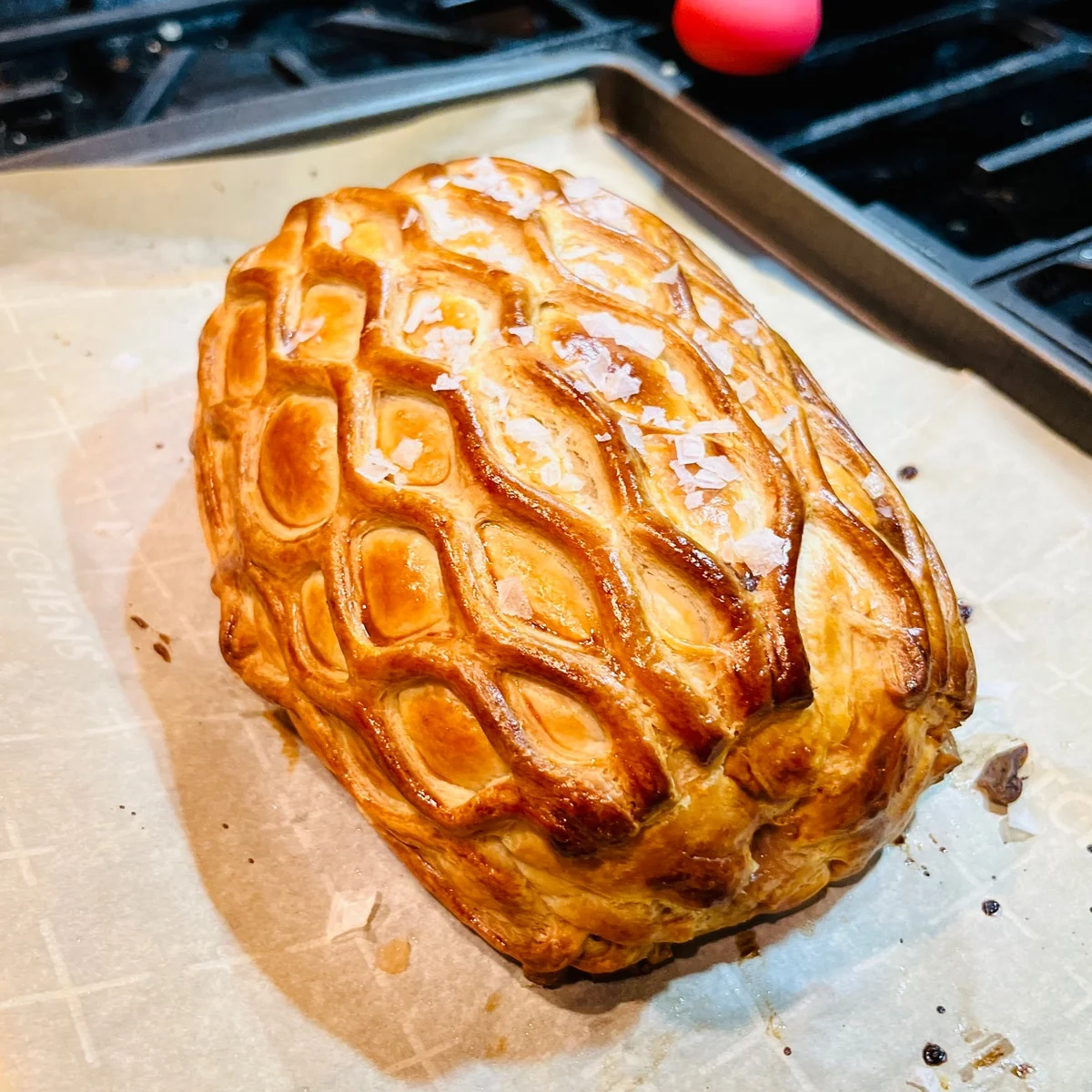 A golden pastry parcel with a lattice pattern on a baking tray.