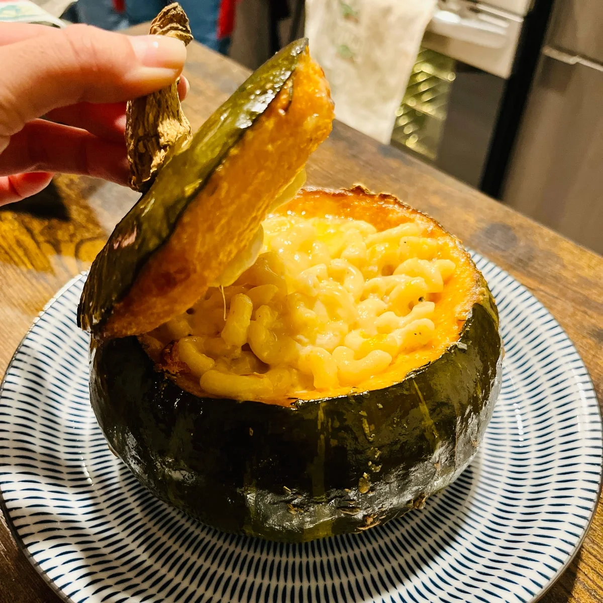A roasted squash filled with pasta, with its lid lifted by hand.