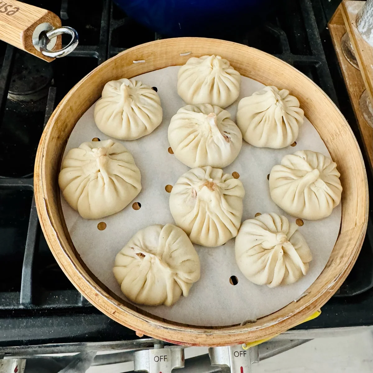 Nine pleated buns arranged in a round bamboo steamer.