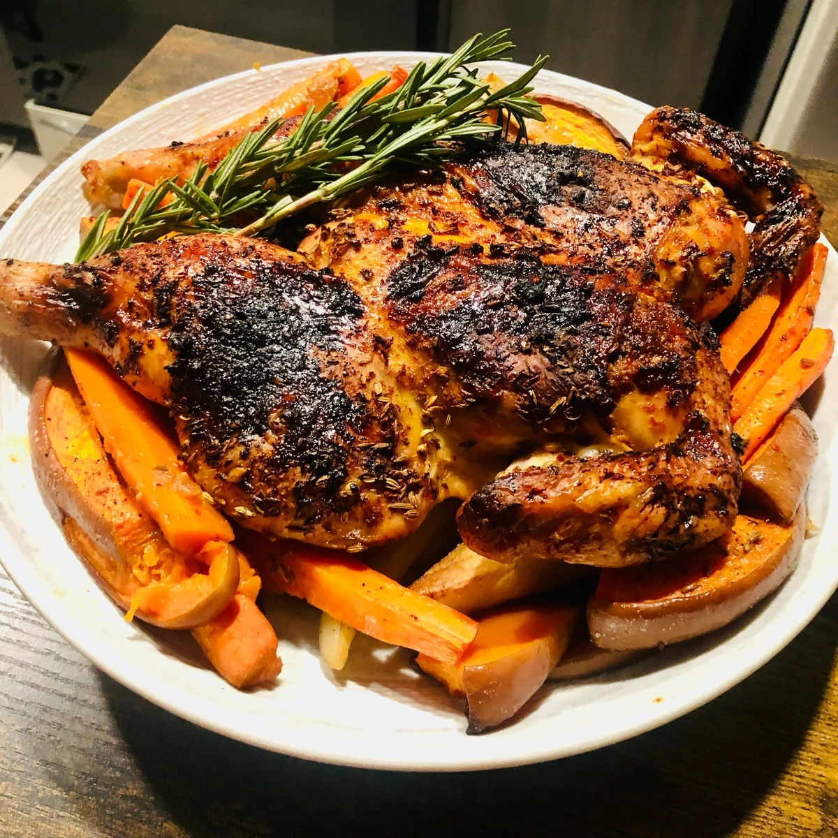 A browned roast chicken on a platter of vegetables, topped with green herb sprigs.